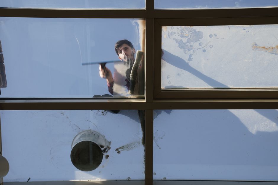 Two professional window cleaners are engaged in surface cleaning and polishing the large glass exterior of a commercial building on Ballards Lane in Finchley, illuminated by natural light. One cleaner